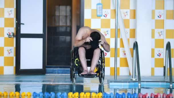 Disabled man in a wheelchair putting on a swimming cap and a goggles. Front angle — Stock Video