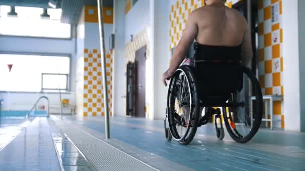 Disabled man is riding in a wheelchair in swimming pool — Stock Video