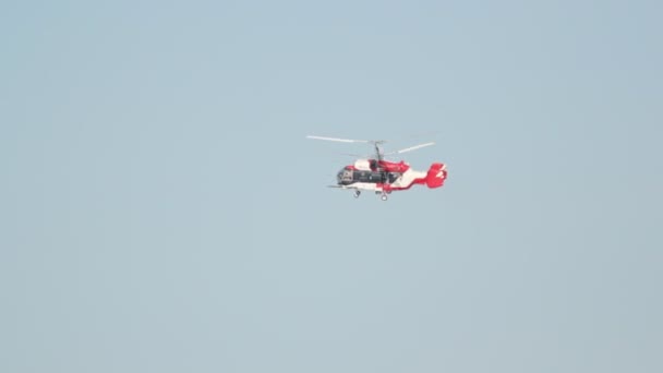 Красно-белый вертолет летает в небе, меняя направление движения — стоковое видео
