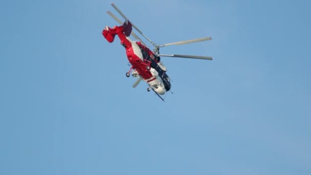Κόκκινο ελικόπτερο που φέρουν κάτω από έναν καθαρό ουρανό χωρίς σύννεφα — Αρχείο Βίντεο