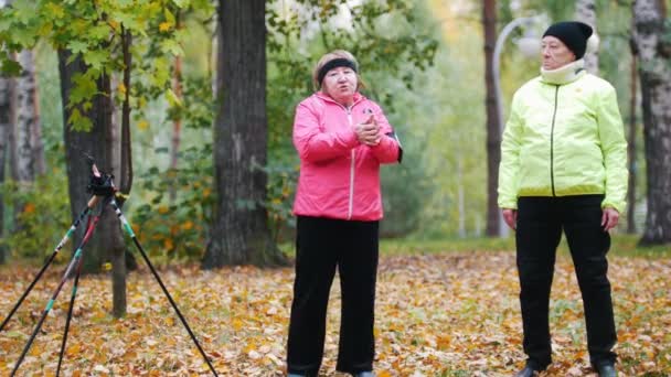 Alte Frau in bunter Jacke steht und wirft Blätter — Stockvideo