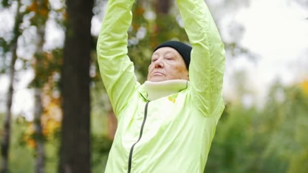 Gammal kvinna i grön jacka gör gymnastik — Stockvideo