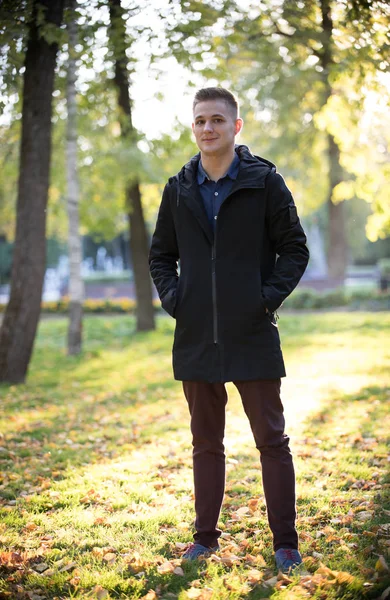 Knappe en jonge man in een zwarte jas staan in het park — Stockfoto