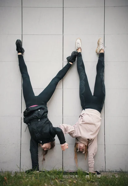 Duas meninas acrobatas de mãos dadas realizando um suporte de mão contra o fundo da parede — Fotografia de Stock