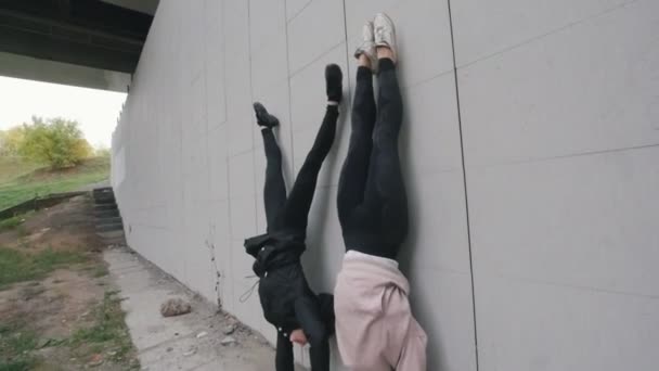 Молодые акробатки стоят на руках у стены — стоковое видео