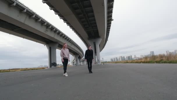 Akrobatische Mädchen springen synchron in einem Spagat in Richtung Kamera auf dem Hintergrund der Brücke — Stockvideo