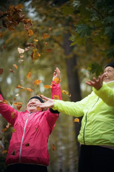 Mujer madura lanzando hojas al aire en un parque de otoño. Mid shot — Foto de Stock