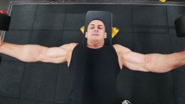 Bir bankta yalan bir dumbbell sinek egzersiz vücut geliştirmeci siyah bir tank top gerçekleştirir