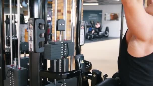 Bodybuilder i ett svart linne utför en övning på axeln dra ner maskiner — Stockvideo