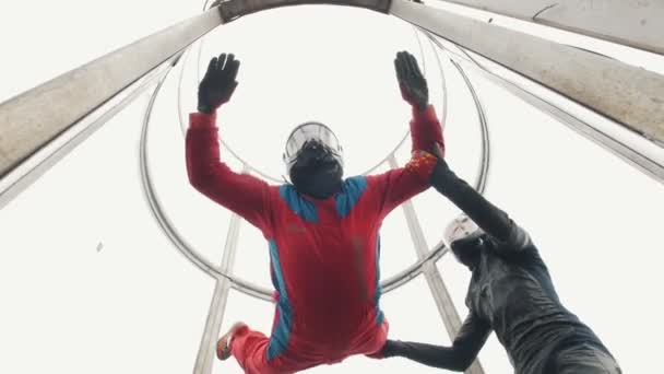 Aerodynamic tube. The wind lifts up the person in red suit. The trainer helping him — Stock Video