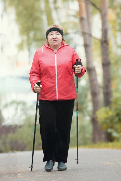 One elderly woman is doing Scandinavian walking in the park. Autumn