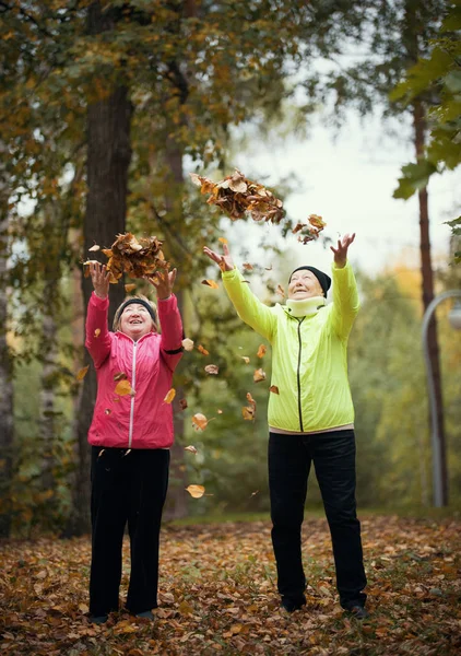 Viejas arrojando hojas al aire en un parque de otoño. Sonriendo. Cuerpo completo — Foto de Stock