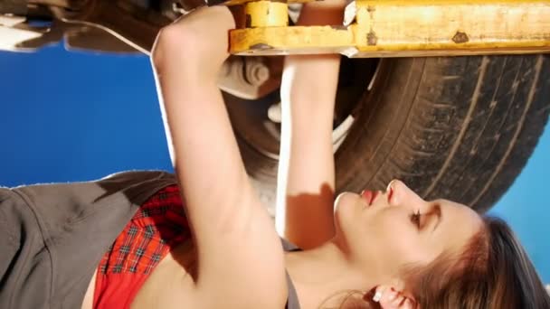 Sexy Mechaniker Mädchen liegt unter dem Auto und repariert es. Seitenwinkel. — Stockvideo