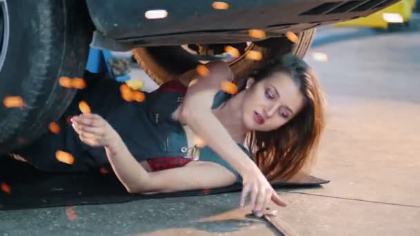 Garota mecânica quente deitada sob o carro e alcançando a chave inglesa. Flocos de fogo . — Vídeo de Stock
