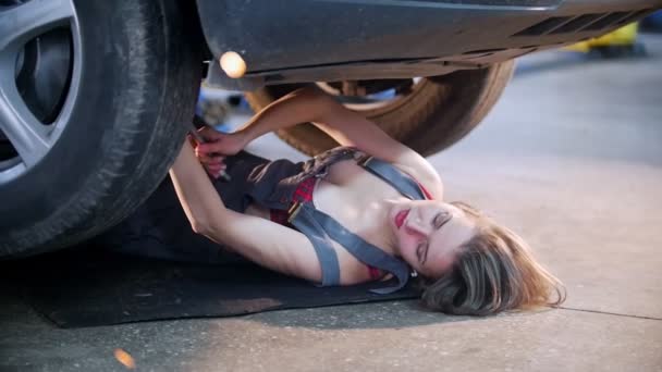 Sexy menina mecânica deitado sob o carro e repará-lo — Vídeo de Stock