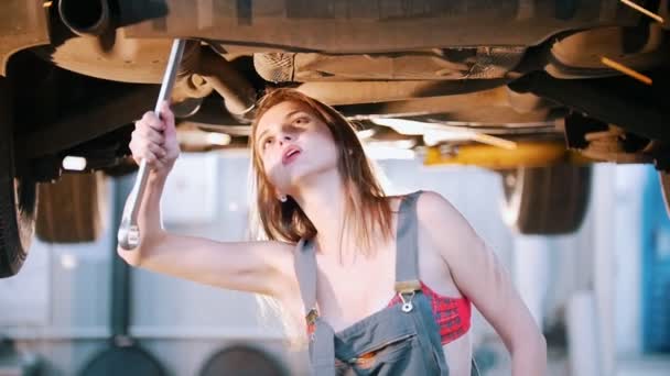 Σέξι κορίτσι μηχανικός κάτω από το αυτοκίνητο επισκευή με ένα κλειδί — Αρχείο Βίντεο