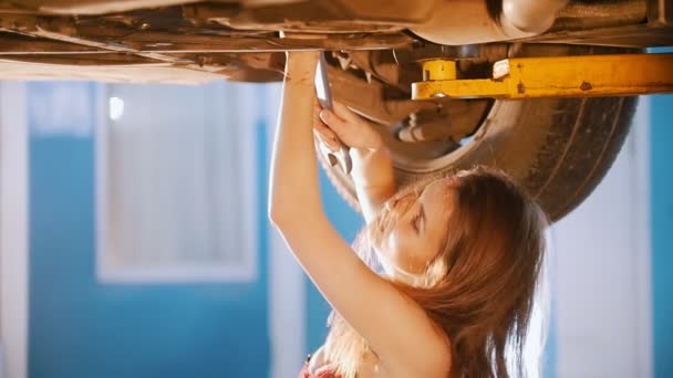 Menina mecânica sexy sob o carro com uma chave de fendas. Atira a cabeça para o lado — Vídeo de Stock