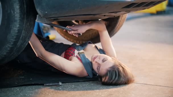 Sexig mekaniker tjej ligga under bilen och nå för nyckeln. Brand flingor. Slow motion — Stockvideo