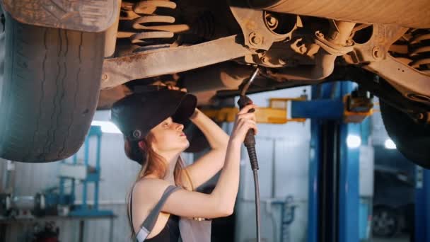 Chica mecánica sexy en un casco repara el coche con una soldadura. Ángulo lateral — Vídeo de stock