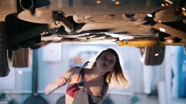 Сексуальная девушка-механик в комбинезоне проходит под машину с гаечным ключом — стоковое видео