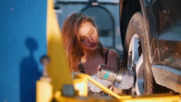 Sexy dívka mechanik v kombinéze s rozcuchanými vlasy šrouby do kola automobilu — Stock video