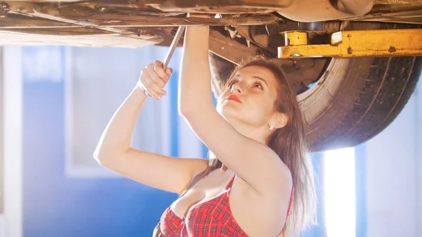 Sexy mechanic meisje onder de auto met een spanner, opzoeken — Stockfoto