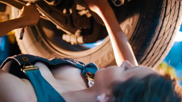 Sexy mechanic meisje legt onder de auto en repareert het met een spanner — Stockfoto