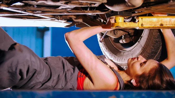Sexy dziewczyna mechanik leżącego pod samochód i je naprawia. Kąt boku — Zdjęcie stockowe