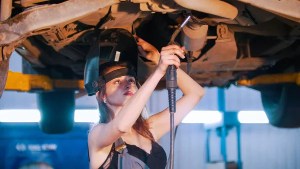 Mechanik dziewczyna w gospodarstwa hełm otwarty spawania maszyny i przynosi to bliżej do samochodu — Zdjęcie stockowe