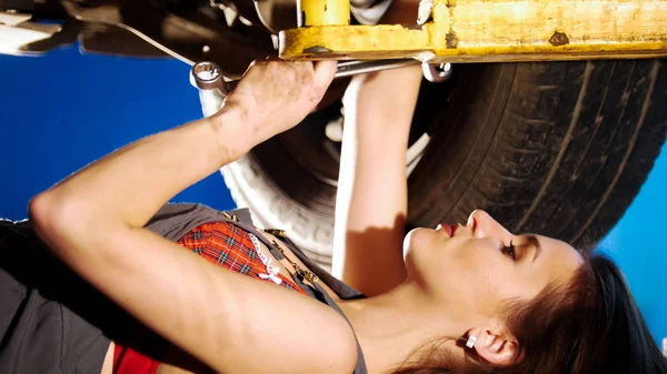 Сексуальная девушка-механик лежит под машиной и чинит ее. Боковой угол. Крупный план — стоковое фото