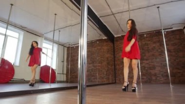 Ayna önünde uçan saç dans pole dans ile kırmızı elbiseli seksi kız durur ve başka bir kutbuna gider