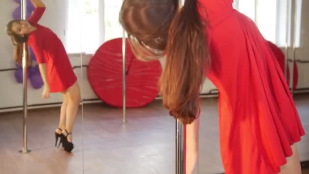 Сексуальная девушка в красном платье с летающими волосами танцует шестом перед зеркалом — стоковое видео