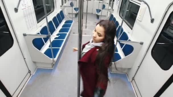 Mujer joven bailando pole dance en tren en movimiento, salta en el poste y cuelga de él — Vídeo de stock