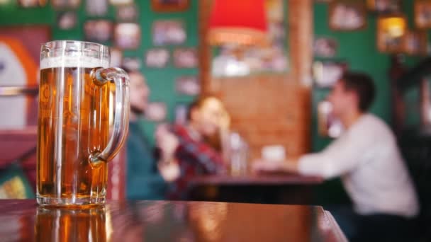 Amigos bebiendo cerveza en el fondo. Una pinta de cerveza en foco — Vídeos de Stock