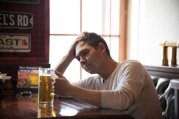 Benadrukt dat de jonge man dranken biertje in de pub. De man houdt het glas — Stockfoto
