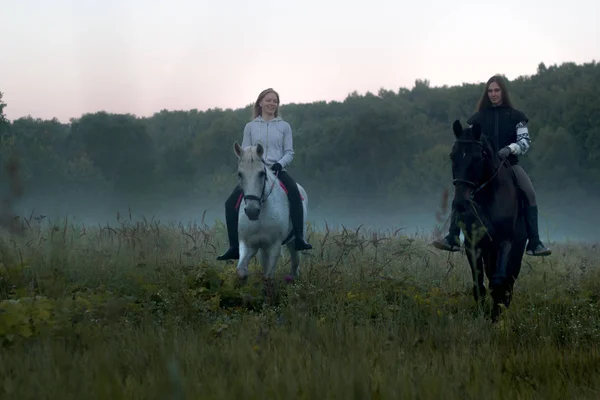 Two women on a foggy field riding horses towards the camera