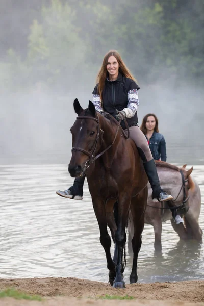 Deux jeunes femmes à cheval sortent du lac — Photo