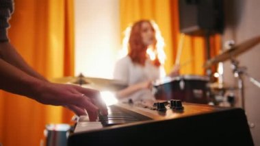 Tekrarlama. Etkileyici kız davulcu ve klavye üzerinde bir adam. Elinden davul için odak. Arka ışık