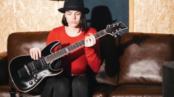 Красивая девушка садится на диван и начинает играть на гитаре — стоковое видео
