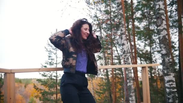 Mujer joven sonriente bailando y saltando en la plataforma. Cabello volador. Bosque en el fondo . — Vídeos de Stock