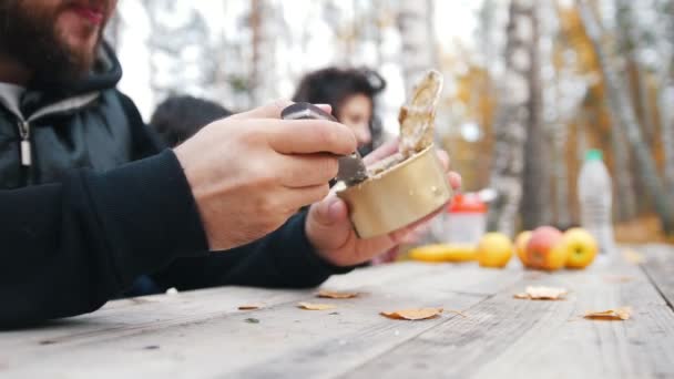 Glücklicher Mann sitzt draußen im Wald am Tisch und genießt sein Dosenfleisch. — Stockvideo