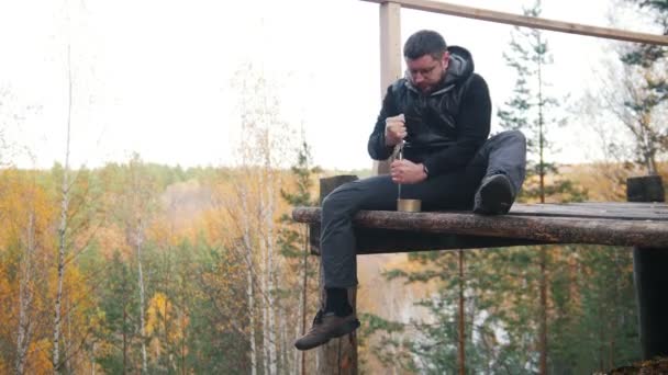 Un hombre se sienta a gran altura y abre la comida enlatada con un cuchillo — Vídeo de stock