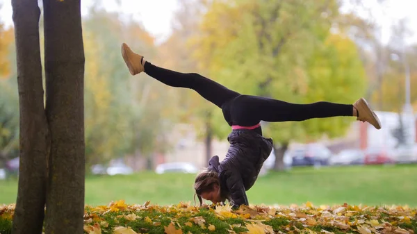 Ragazza che esegue ginnasta in piedi sulle mani. Parco, autunno — Foto Stock