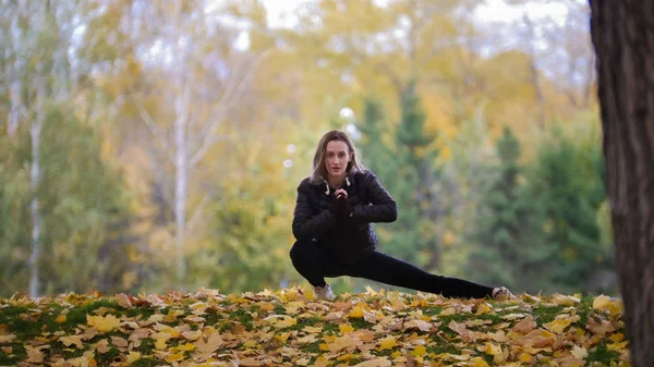 Gymnastka dívka táhnoucí se jí nohy v podzimním parku — Stock fotografie