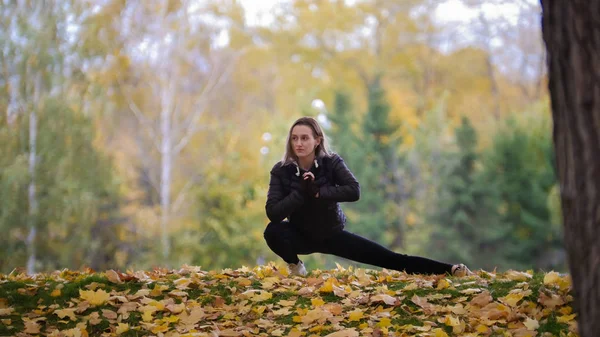 Gymnastka dívka táhnoucí se jí nohy v podzimním parku, při pohledu na stranu — Stock fotografie