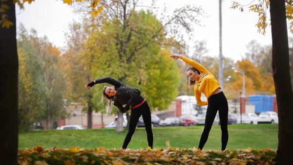 Chicas calentándose afuera antes de entrenar en el parque. Inclinarse a la izquierda —  Fotos de Stock