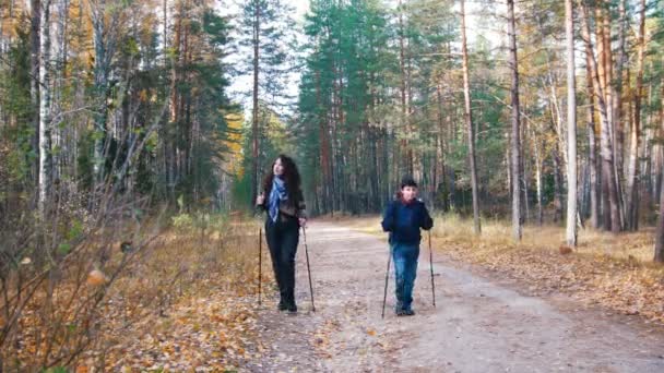 Jonge vrouw en een jongen op Scandinavische lopen in het bos. Camping — Stockvideo