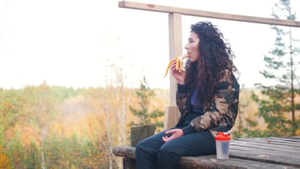 Una mujer se sienta en una plataforma de altitud y come plátano . — Vídeo de stock