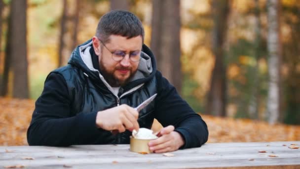 Ένας άνθρωπος που κάθεται στο τραπέζι και τρώει κονσέρβες βρασμένο κρέας χρησιμοποιώντας ένα μαχαίρι. — Αρχείο Βίντεο