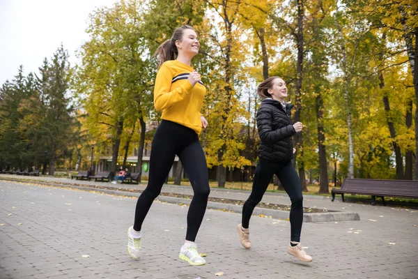 Two girls jogging in autumn park and smiling